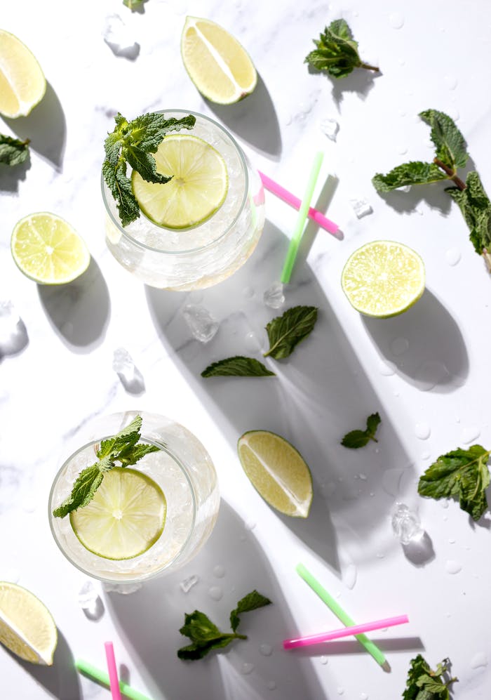 Overhead view of lemon-mint beverages with fresh lime slices and mint leaves on a white background.
